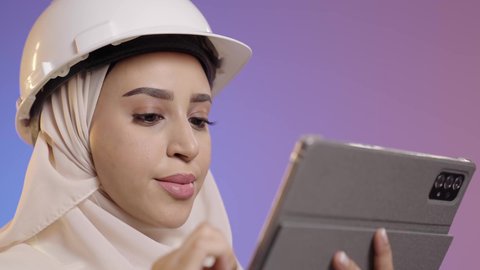 التأكد من سير الأعمال بالشكل المطلوب والصحيح، كتابة آخر المستجدات حول المشروع، بورتريه مقرب لمهندسة عربية خليجية سعودية ترتدي الحجاب والخوذة وسترة الحماية تقوم باستخدام الجهاز اللوحي، الأجهزة التقنية الحديثة، تدوين و تسجيل الملاحظات, خلفية ملونه