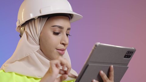 كتابة آخر المستجدات حول المشروع، التأكد من سير الأعمال بالشكل المطلوب والصحيح، بورتريه مقرب لمهندسة عربية خليجية سعودية ترتدي الحجاب والخوذة وسترة الحماية تقوم باستخدام الجهاز اللوحي، الأجهزة التقنية الحديثة، تدوين و تسجيل الملاحظات, خلفية ملونه