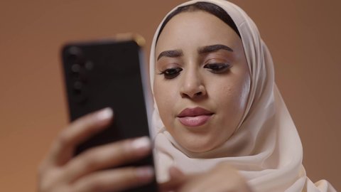 التواصل الاجتماعي مع الأقارب والأصدقاء عبر الجوال، استخدام جهاز تقني حديث ومتطور، بورتريه مقرب لشابة عربيه خليجيه سعودية ترتدي الحجاب و العباءة تمسك بيدها الهاتف المحمول، خلفية ملونه