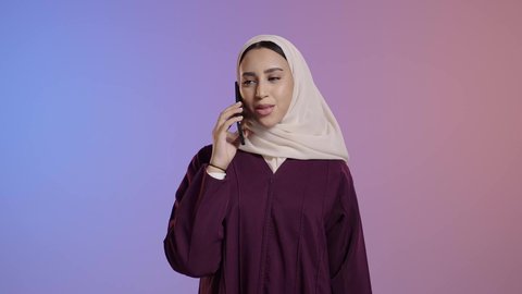 مفهوم صلة الرحم، دمج التكنولوجيا والتقنية الحديثة في الحياة اليومية، بورتريه لامرأة عربية خليجية سعودية محجبة ترتدي العباءة تقوم بإجراء مكالمة صوتية عبر الجوال، التواصل مع الأهل والأصدقاء، خلفية ملونه