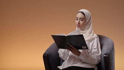 استثمار وقت الفراغ في التعلم والاطلاع، هواية القراءة والاستكشاف، مفهوم التثقيف والبحث العلمي، بورترية لشابة عربية خليجية سعودية ترتدي العباية والحجاب تجلس على كرسي تقوم بقراءة كتاب ما، خلفية ملونه