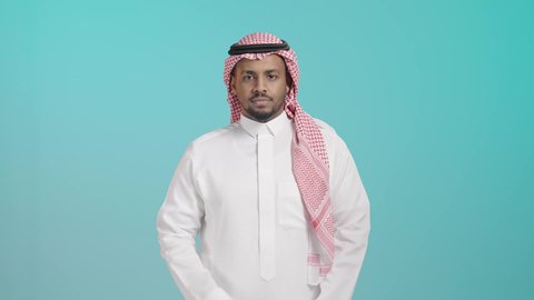 مفهوم الاناقه والرجولة، الاهتمام بالمظهر الخارجي، بورتريه لرجل عربي خليجي سعودي مبتسم يرتدي الشماغ و الثوب التقليدي يقف بأيدي متقاطعه ينظر إلى الكاميرا بتعابير الثقة بالنفس ,خلفية خضراء