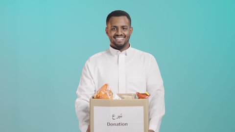 الأعمال الخيرية الإسلاميه، المساعدات والتبرعات الإنسانية، الاحساس بالأخرين ومساعدتهم، بورتريه لرجل عربي خليجي سعودي مبتسم يرتدي الثوب التقليدي  يحمل بيده صندوق تبرع، خلفية خضراء