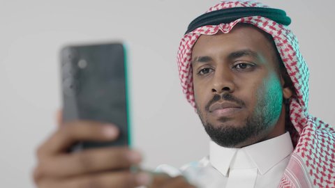تصفح مواقع التواصل الاجتماعي، بورترية مقرب لرجل عربي خليجي سعودي يرتدي الثوب التقليدي و الشماغ  يمسك بيده الهاتف المحمول، الدردشة والتواصل مع الأهل و الأصدقاء، استخدام جهاز تقني حديث ومتطور، العمل عن بعد وانجاز المهام المطلوبة، خلفية رمادية