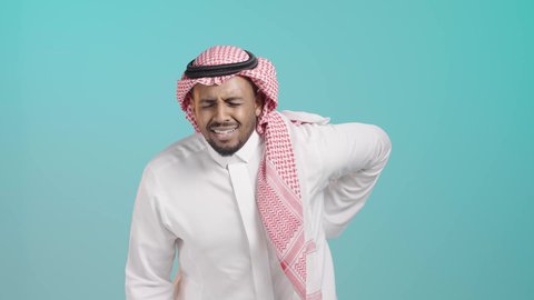 الحاجة إلى العلاج، آلام الظهر والعامود الفقري، التعب والإرهاق والإحساس بالمرض، بورتريه لرجل عربي خليجي سعودي يرتدي الثوب الابيض و الشماغ يضع يده على ظهره، إيماءات وجه ويدين تدل على الوجع والألم، خلفية خضراء