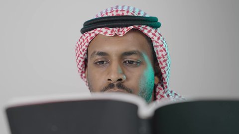 دراسة محتوى الكتب بتمعن، ثقافة التعلم الذاتي ، بوترية مقرب  لشاب عربي خليجي سعودي يرتدي الثوب الابيض و الشماغ يحمل بيده كتاب تثقيفي ، إيماءات التركيز والاندماج ، الاستمتاع بقراءة الروايات والقصص، خلفية رمادية