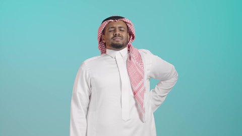 آلام الظهر والعامود الفقري، التعب والإرهاق والإحساس بالمرض، بورتريه لرجل عربي خليجي سعودي يرتدي الثوب الابيض و الشماغ يضع يده على ظهره، إيماءات وجه ويدين تدل على الوجع والألم، الحاجة إلى العلاج، خلفية خضراء