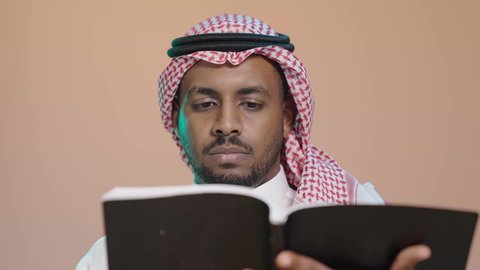ثقافة التعلم الذاتي، قراءة الكتب بتمعن ، بوترية مقرب لشاب عربي خليجي سعودي يرتدي الثوب الابيض و الشماغ يحمل بيده كتاب تثقيفي ، إيماءات التركيز والاندماج ، الاستمتاع بقراءة الروايات والقصص، خلفية بنية