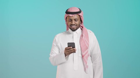 تصفح التطبيقات وبرامج التواصل الاجتماعي، العمل عن بعد، استخدام جهاز تقني حديث ومتطور، التواصل وتبادل الأحاديث والأخبار مع الأهل والأصدقاء عبر الدردشة، بورترية لرجل عربي خليجي سعودي يرتدي الثوب الابيض و الشماغ يمسك بيده الهاتف المحمول، خلفية خضراء