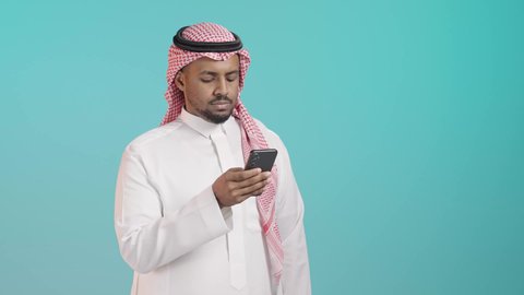 العمل عن بعد، استخدام جهاز تقني حديث ومتطور، التواصل وتبادل الأحاديث والأخبار مع الأهل والأصدقاء عبر الدردشة، بورترية مقرب لرجل عربي خليجي سعودي يرتدي الثوب الابيض و الشماغ يمسك بيده الهاتف المحمول، تصفح التطبيقات وبرامج التواصل الاجتماعي، خلفية خضراء