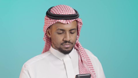 استخدام جهاز تقني حديث ومتطور، التواصل وتبادل الأحاديث والأخبار مع الأهل والأصدقاء عبر الدردشة، بورترية مقرب لرجل عربي خليجي سعودي يرتدي الثوب الابيض و الشماغ يمسك بيده الهاتف المحمول، العمل عن بعد، تصفح التطبيقات وبرامج التواصل الاجتماعي، خلفية خضراء