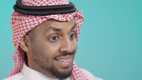 Communicating with family and friends, making a video call via mobile phone, a close-up portrait of a Saudi Arabian Gulf man wearing traditional attire and a ghutrah broadcasting live via mobile, using modern technological devices, green background.