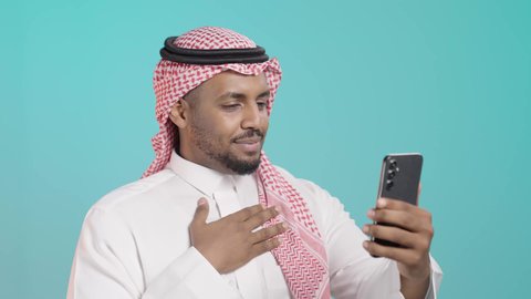 اجراء مكالمة فيديو عبر الهاتف المحمول، بورترية مقرب لرجل عربي خليجي سعودي يرتدي الثوب التقليدي والشماغ يقوم ببث مباشر عبر الموبايل، التواصل مع الأهل والاصدقاء، استخدام الأجهزة التقنية الحديثة، خلفية خضراء