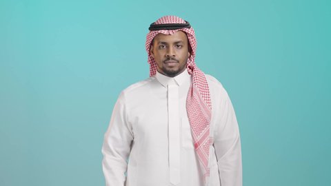 إشارات تدل على النهي والمنع، الرفض والامتناع والانزعاج, بورتريه لشاب عربي خليجي سعودي يرتدي الثوب الابيض و الشماغ ينظر الى الكاميرا يمد يديه نحو الأمام مع رفع الكف بتعابير النهي عن فعل امر ما, خلفية خضراء