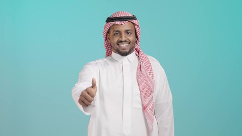 مفهوم القبول والموافقه، تعابير الإعجاب والرضى، بورتريه مقرب لرجل عربي خليجي سعودي يرتدي الزي التقليدي يرفع اصبع الابهام بإيماءات الامتياز والجودة، خلفية خضراء