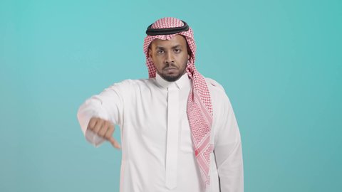 القلق والفشل في تحقيق أمر ما، الإشارة بإصبع الإبهام للاسفل دليل الرفض، حركة يد وايماءات وجه تدل على عدم الإعجاب والموافقة، بورتريه لرجل عربي خليجي سعودي يرتدي الثوب الابيض و الشماغ تظهر عليه علامات عدم القبول، خلفية خضراء