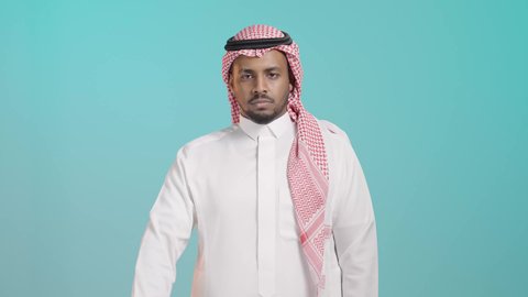 الإشارة بإصبع الإبهام للاسفل دليل الرفض، حركة يد وايماءات وجه تدل على عدم الإعجاب والموافقة، بورتريه لرجل عربي خليجي سعودي يرتدي الثوب الابيض و الشماغ تظهر عليه علامات عدم القبول، خلفية خضراء