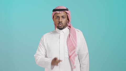 حركة يد تدل على الصمت، الهدوء والسكون وعدم الإزعاج، بورتريه لرجل عربي خليجي اماراتي يرتدي  الثوب الابيض و المشاغ يضع أصبع السبابة على فمه بإيماءات طلب السكوت والصمت، خلفية خضراء