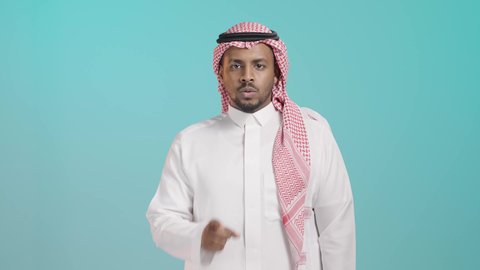 الهدوء والسكون وعدم الإزعاج، التوقف عن الكلام وخفض الصوت، بورتريه لرجل عربي خليجي اماراتي يرتدي  الثوب الابيض و المشاغ يضع أصبع السبابة على فمه بإيماءات طلب السكوت والصمت، خلفية خضراء