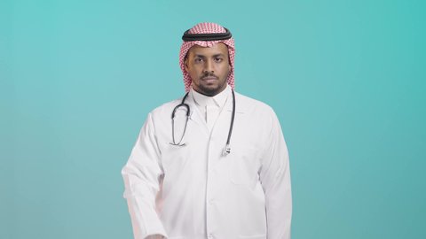إشارة رفض وعدم السماح بالمرور, بورتريه لطبيب عربي خليجي سعودي يرتدي المعطف الطبي و السماعات و الشماغ ينظر الى الكاميرا و يشير بيده لطلب التوقف والابتعاد، خلفية خضراء