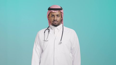 تقديم الخدمات الصحية، بورتريه لطبيب عربي خليجي سعودي يرتدي المعطف و السماعات الطبية و الشماغ، مفهوم الطب والرعاية الصحية، ايماءات وجه سعيد ويدين تدل على القبول والموافقة، خلفية خضراء