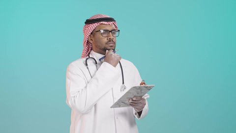 توثيق الملاحظات الصحية, ايماءات التفكير فى شيء ما, العمل في القطاع الصحي في المملكة العربية السعودية، بورترية لطبيب عربي خليجي سعودي يرتدي المعطف و السماعة الطبية و الشماغ يقوم بكتابة تقرير طبي , خلفية خضراء