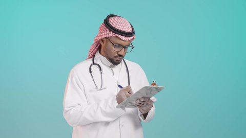 تدوين الملاحظات الطبية, ايماءات التفكير فى شيء ما, العمل في القطاع الصحي في المملكة العربية السعودية، بورترية لطبيب عربي خليجي سعودي يرتدي المعطف و السماعة الطبية و الشماغ يقوم بكتابة تقرير طبي , خلفية خضراء