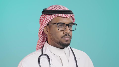 تسجيل بيانات المرضى, ايماءات التفكير فى شيء ما, العمل في القطاع الصحي في المملكة العربية السعودية، بورترية مقرب لطبيب عربي خليجي سعودي يرتدي المعطف و السماعة الطبية يقوم بكتابة تقرير طبي , خلفية خضراء