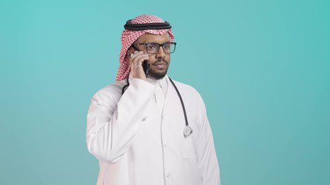 الطب الحديث والاستشارات الرقمية, تقديم الخدمات للمرضى بكل كفاءه, مفهوم الطب والرعاية الصحية, بورترية لطبيب عربي خليجي سعودي يرتدي المعطف الابيض و السماعات الطبية يتحدث بالهاتف المحمول  و يقوم بمراجعة الملاحظات، خلفية  خضراء