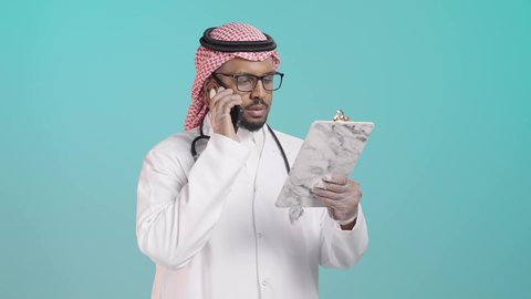 متابعة الحالات المرضية عن بعد, تقديم الخدمات للمرضى بكل كفاءه, مفهوم الطب والرعاية الصحية, بورترية لطبيب عربي خليجي سعودي يرتدي المعطف الابيض و السماعات الطبية يتحدث بالهاتف المحمول  و يقوم بمراجعة الملاحظات، خلفية  خضراء