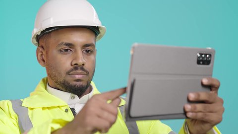 استخدام جهاز تقني حديث متطور، تصفح مواقع التواصل الاجتماعي، مفهوم الهندسة والإنشاء المعماري، مراجعة المخططات عبر الجهاز اللوحي، بورتريه مقرب لمهندس عربي خليجي سعودي يرتدي ستره و خوذة الحماية يمسك بيده جهاز التابليت المحمول، خلفية خضراء