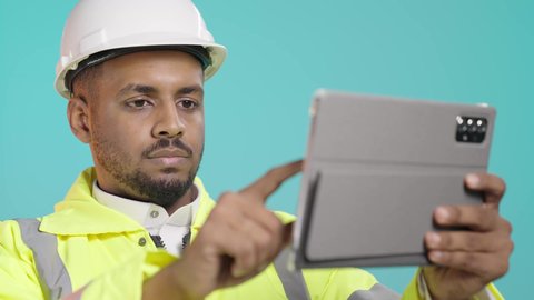 مفهوم الهندسة والإنشاء المعماري، مراجعة المخططات عبر الجهاز اللوحي, تصفح مواقع التواصل الاجتماعي، استخدام جهاز تقني حديث متطور، بورتريه مقرب لمهندس عربي خليجي سعودي يرتدي ستره و خوذة الحماية يمسك بيده جهاز التابليت المحمول، خلفية خضراء