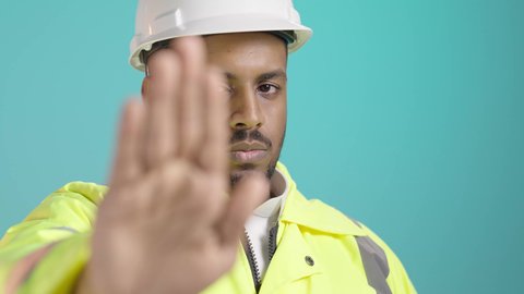 طلب التوقف وعدم الاقتراب، الرفض والامتناع والانزعاج, مفهوم الهندسة والانشاءات المعمارية، العمل في القطاع الهندسي، بورتريه مقرب لمهندس عربي خليجي سعودي يرتدي سترة الحماية و الخوذة يمد يرفع كفه نحو الأمام بإيماءات النهي, خلفية خضراء