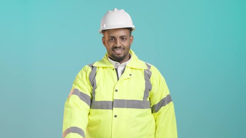 The concept of acceptance and approval, expressions of admiration and satisfaction, a portrait of a smiling Saudi Gulf Arab engineer wearing a jacket and safety helmet, raising his thumb with gestures of excellence and quality, green background.