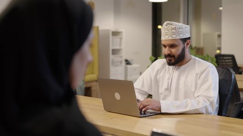 استخدام الحاسوب المحمول, مراجعة الخطط والاستراتيجيات والاتفاقيات عبر التقنيات الحديثه، توفير بيئة عمل مريحة ومناسبة، إنجاز مهام الاعمال باحترافية، مهن ووظائف ادارية مكتبية, رجل عربي خليجي عماني يرتدي الدشداشة و الكمة يعمل على اللابتوب في المكتب