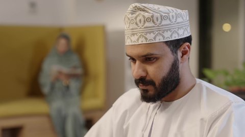 النقر والتفاعل مع لوحة المفاتيح, دمج التقنية والتكنولوجيا في الحياة العملية، إنجاز مهام الاعمال باحترافية، مهن ووظائف ادارية مكتبية, رجل عربي خليجي عماني يرتدي الدشداشة و الكمة يعمل على اللابتوب في المكتب