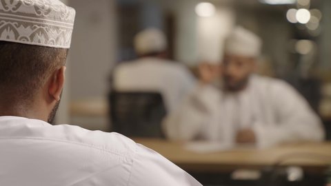 استخدام الاوراق البيضاء الفارغة في العمل، تدوين وتسجيل الملاحظات والمعلومات على الورق, إدارة الأعمال وتنظيمها،  رجل عربي خليجي عماني يرتدي الدشداشة و الكمة يقوم بالكتابة, ايماءات التفكير و الانهماك