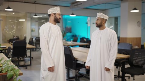 مفهوم الإدارة المتعاونة، عقد صفقات عمل جديدة ناجحة بين رجال الأعمال،  فريق عمل داخل غرفة الاجتماعات في مقر الشركة, رجلان عربيان خليجيان عمانيان يرتديان الدشداشة والكمة يقومان بمصافحة و تحية بعضهما