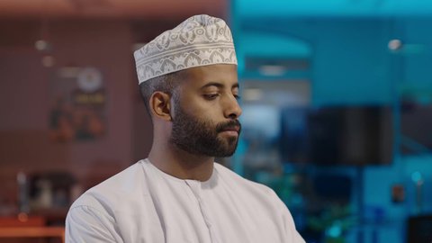 الكتابة باستخدام لوحة المفاتيح، دمج الأعمال مع التقنية والتكنولوجيا الحديثة والمتطورة، النظر إلى الكاميرا بتعابير السعادة والسرور, مهن و وظائف ادارية مكتبية, رجل عربي خليجي عماني يرتدي الدشداشة و الكمة يعمل على اللابتوب في المكتب، إنجاز المهام العمل المطلوبة