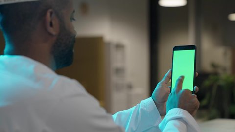 تصفح مواقع التواصل الاجتماعي عبر الانترنت، استخدام الهاتف المحمول في العمل، بورتريه من الخلف لرجل عربي خليجي عماني يرتدي الدشداشة و الكمة يعمل من خلال الموبايل, الاستفادة من الأجهزة التكنولوجية الحديثة والمتطورة