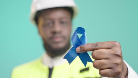 بورتريه مقرب لشريطة الجودة, العمل في القطاع الهندسي، المهارة و اتقان المهام, مهندس أسمر عربي خليجي سعودي يرتدي الخوذه و سترة الحماية و يمسك شريط أزرق و يقربه للكاميرا, مهن ووظائف سعودية، خلفية زرقاء