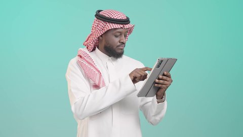 هواية المطالعة والاستكشاف وقضاء وقت الفراغ بالتعلم والثقافة، تصفح مواقع التواصل الاجتماعي، التطور التكنولوجي في مختلف المجالات, استخدام التقنيات الحديثة في العمل عن بعد، بورتريه لرجل أسمر عربي خليجي سعودي مبتسم يرتدي الثوب التقليدي و الشماغ و يمسك التابلت, خلفية زرقاء
