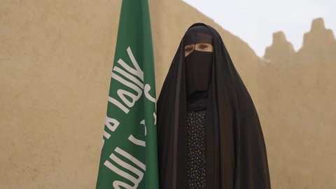 الاحتفال باليوم الوطني 23 سبتمبر, ذكرى يوم التأسيس 22 فبراير, سيدة عربية خليجية سعودية ترتدي العباءة السوداء والبرقع وتقف بجانب العلم, يوم العلم السعودي 11 مارس, التفاخر بالإنتماء للوطن, ارتداء الأزياء الشعبية التقليدية في المناسبة الوطنية
