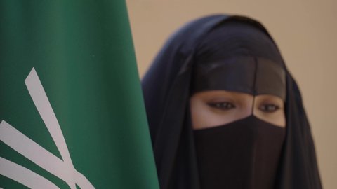 الاحتفال باليوم الوطني 23 سبتمبر, ذكرى يوم التأسيس 22 فبراير, سيدة عربية خليجية سعودية ترتدي العباءة السوداء والبرقع وتقف بجانب العلم, يوم العلم السعودي 11 مارس, التفاخر بالإنتماء للوطن, ارتداء الأزياء الشعبية التقليدية في المناسبة الوطنية