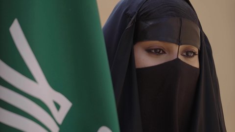 الاحتفال باليوم الوطني 23 سبتمبر, ذكرى يوم التأسيس 22 فبراير, سيدة عربية خليجية سعودية ترتدي العباءة السوداء والبرقع وتقف بجانب العلم, يوم العلم السعودي 11 مارس, التفاخر بالإنتماء للوطن, ارتداء الأزياء الشعبية التقليدية في المناسبة الوطنية