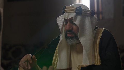 الفخر بأصالة المملكة، ارتداء الزي الشعبي في المناسبة الوطنية، تصوير مقرب لرجل عربي خليجي سعودي يرتدي الغترة والعقال الذهبي والبشت يمسك بيده الريشة يقوم بالكتابة على مخطوطة جلد تاريخية، الخطابات والمراسلات التراثية لتأسيس الدولة الأولى 1727م، يوم بدينا 22 فبراير