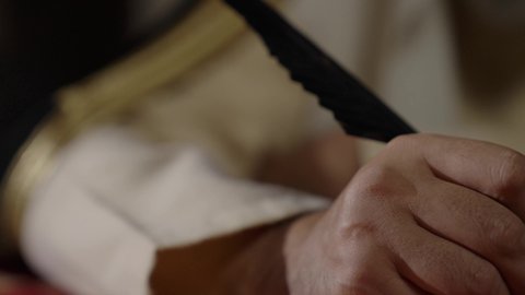 ارتداء الزي الشعبي في المناسبة الوطنية، تصوير مقرب لرجل عربي خليجي سعودي يرتدي الغترة والعقال الذهبي والبشت يمسك بيده الريشة يقوم بالكتابة على مخطوطة جلد تاريخية، الخطابات والمراسلات التراثية لتأسيس الدولة الأولى 1727م، يوم بدينا 22 فبراير، الفخر بأصالة المملكة