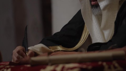 الفخر بأصالة المملكة، ارتداء الزي الشعبي في المناسبة الوطنية، تصوير مقرب لرجل عربي خليجي سعودي يرتدي الغترة والعقال الذهبي والبشت يمسك بيده الريشة يقوم بالكتابة على مخطوطة جلد تاريخية، الخطابات والمراسلات التراثية لتأسيس الدولة الأولى 1727م، يوم بدينا 22 فبراير