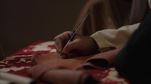 Pride in the authenticity of the Kingdom, wearing traditional dress on the national occasion, a close-up of a Saudi Arabian Gulf man wearing a ghutra, golden agal and bisht holding a pen in his hand writing on a historical leather manuscript, heritage letters and correspondence for the establishment of the first state in 1727 AD, the day we began, February 22
