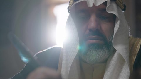 The day we began, February 22, pride in the authenticity of the Kingdom, wearing traditional dress on the national occasion, a close-up of a Saudi Arabian Gulf man wearing a ghutra, a golden agal, and a bisht, holding a pen in his hand, writing on a historical leather manuscript, heritage letters and correspondence for the establishment of the first state in 1727 AD